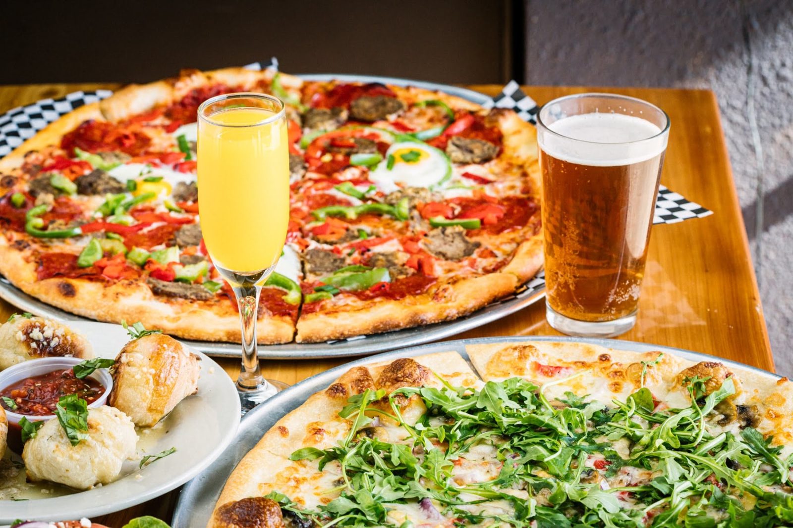 Pizzas, garlic knots, a mimosa and a pint on the table at Warpath Pizza & Pub